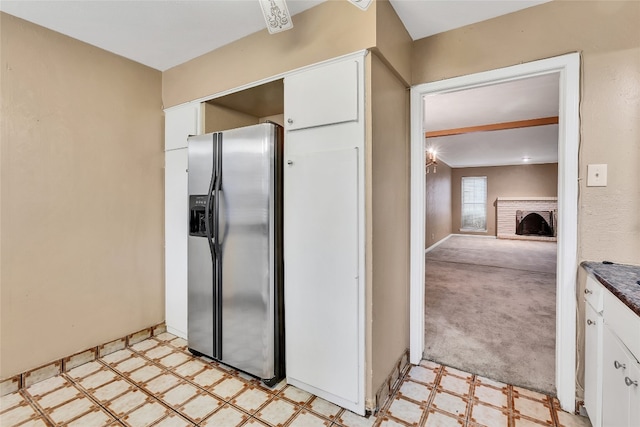 kitchen featuring light colored carpet, white cabinetry, stainless steel refrigerator with ice dispenser, and a fireplace