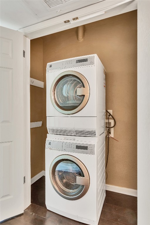 clothes washing area with stacked washer / dryer and dark wood-type flooring