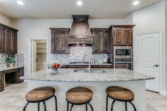 kitchen featuring appliances with stainless steel finishes, a center island with sink, and light stone countertops