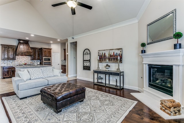 living room featuring high vaulted ceiling, light wood-type flooring, ceiling fan, ornamental molding, and sink