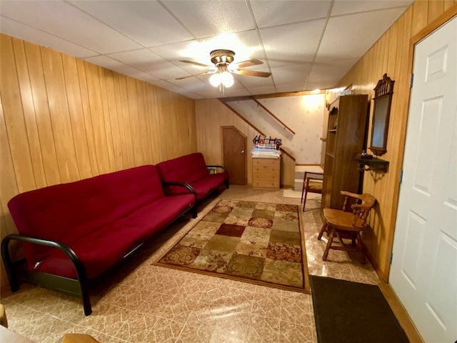 tiled living room featuring a paneled ceiling, wood walls, and ceiling fan