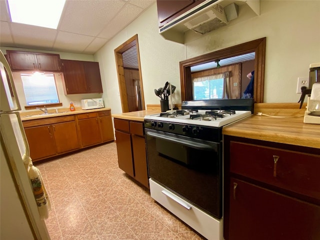 kitchen with light tile flooring, custom range hood, a drop ceiling, white appliances, and a wealth of natural light