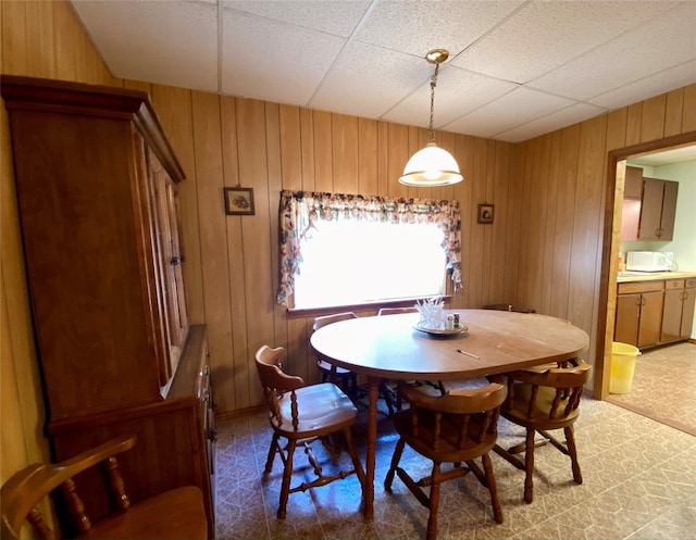 tiled dining room featuring a paneled ceiling and wooden walls