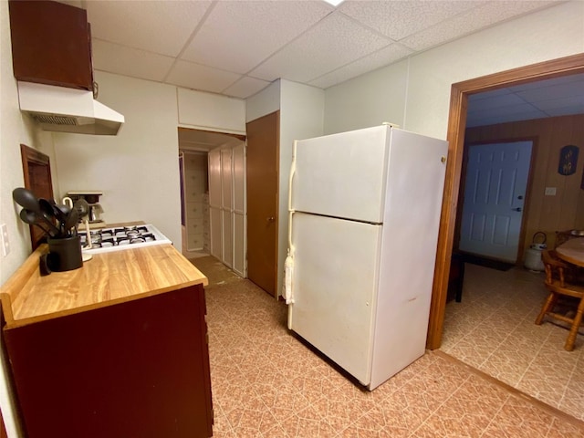 kitchen featuring premium range hood, white refrigerator, light tile floors, wooden counters, and a paneled ceiling