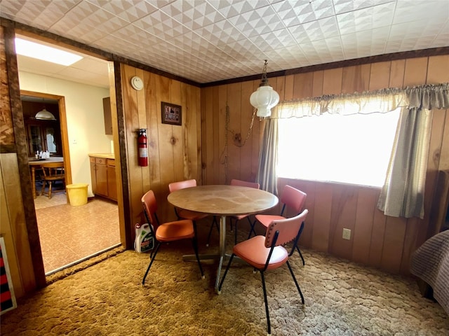 carpeted dining area featuring wood walls