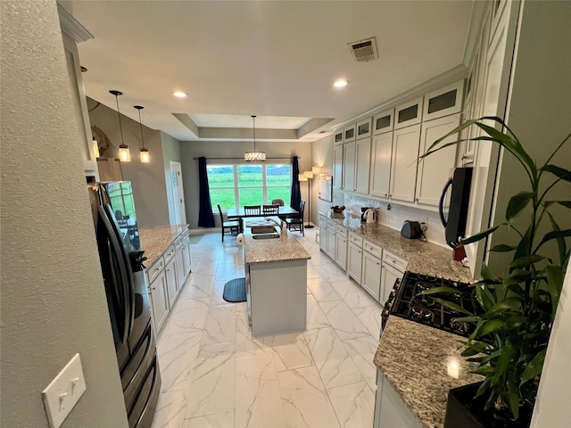 kitchen featuring a kitchen island with sink, fridge with ice dispenser, decorative light fixtures, light stone countertops, and a tray ceiling