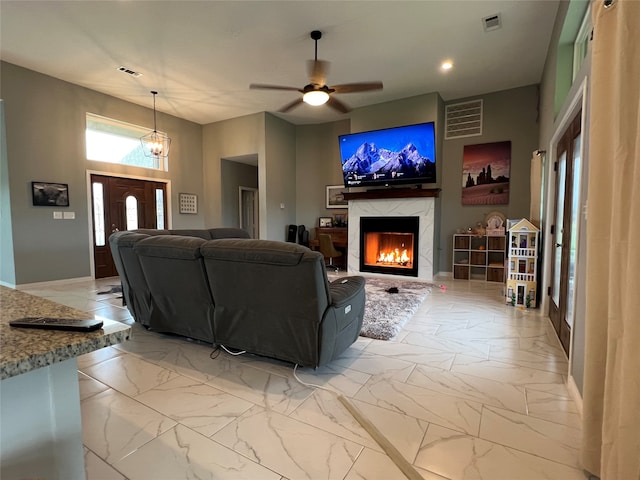 living room featuring a high end fireplace and ceiling fan with notable chandelier