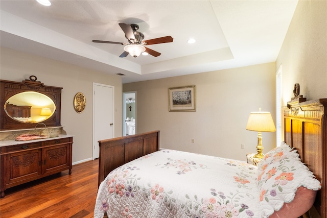 bedroom with dark hardwood / wood-style flooring, ceiling fan, and a raised ceiling