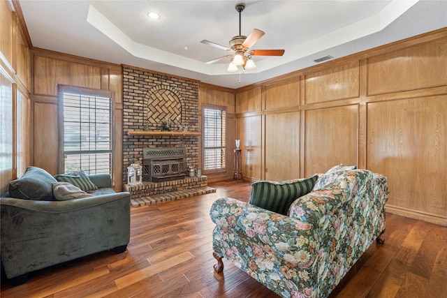 living room with a raised ceiling, ceiling fan, dark hardwood / wood-style flooring, and a fireplace