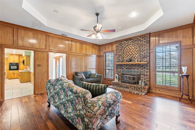 living room featuring ceiling fan, a fireplace, hardwood / wood-style flooring, and a tray ceiling