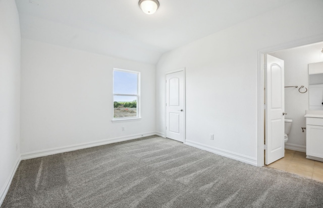 unfurnished bedroom featuring light carpet, connected bathroom, and vaulted ceiling