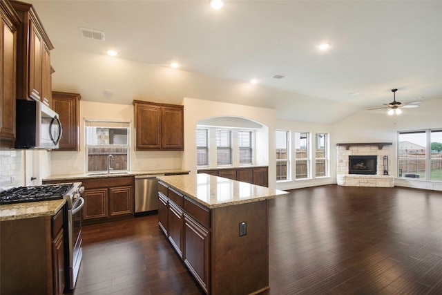 kitchen featuring a center island, tasteful backsplash, a stone fireplace, appliances with stainless steel finishes, and dark hardwood / wood-style floors