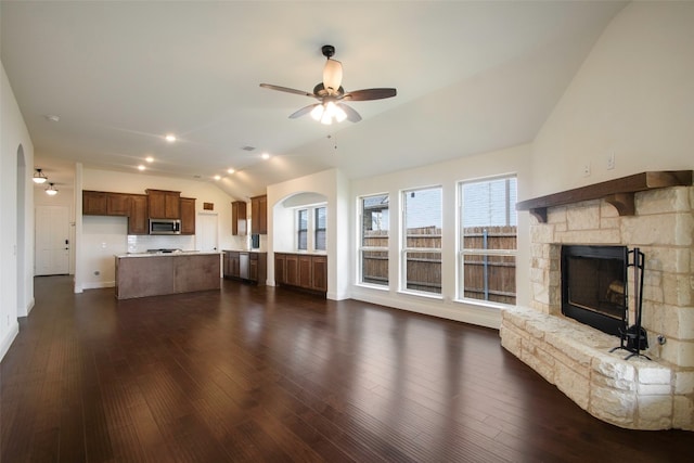 unfurnished living room with ceiling fan, dark wood-type flooring, vaulted ceiling, and a stone fireplace