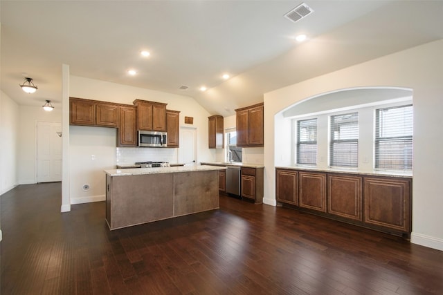 kitchen with backsplash, dark wood-type flooring, stainless steel appliances, a center island, and light stone counters