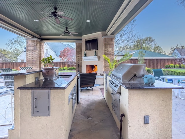 view of terrace featuring an outdoor fireplace, ceiling fan, an outdoor kitchen, grilling area, and sink