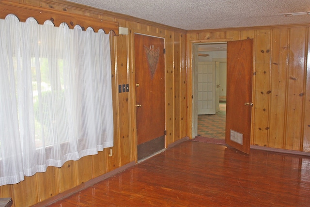 unfurnished room featuring a textured ceiling, dark hardwood / wood-style flooring, and wooden walls