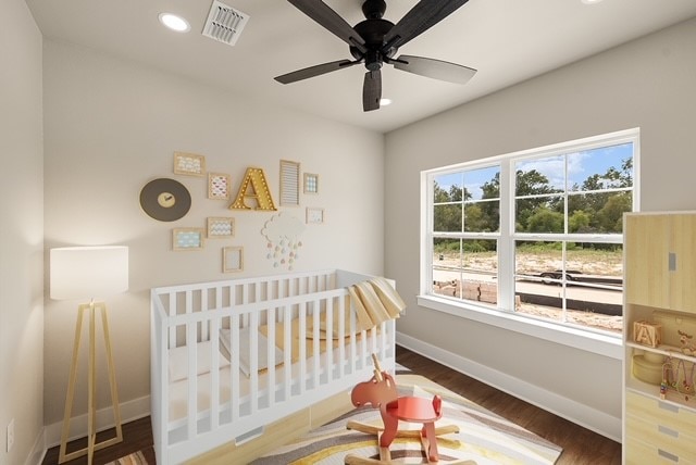 bedroom featuring a crib, ceiling fan, and dark hardwood / wood-style floors