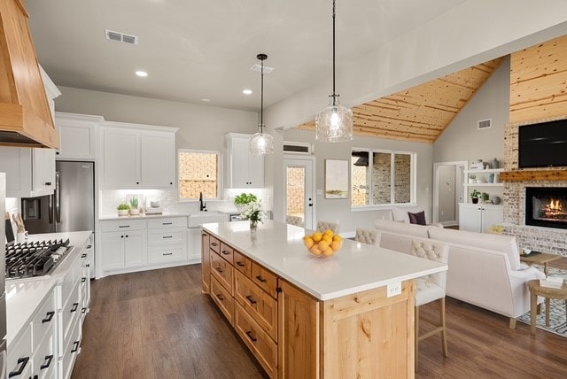 kitchen with lofted ceiling with beams, white cabinetry, a brick fireplace, dark wood-type flooring, and a center island