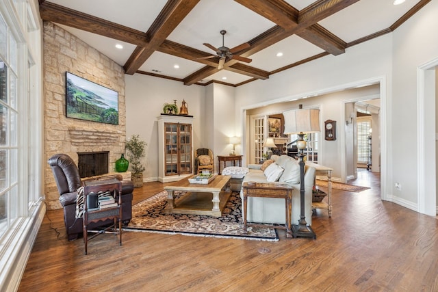 living room featuring wood-type flooring, a stone fireplace, coffered ceiling, and ceiling fan