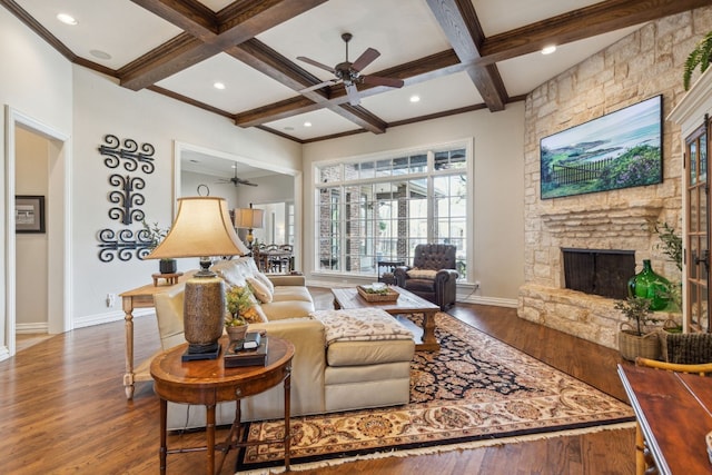 living room with beam ceiling, wood-type flooring, a stone fireplace, coffered ceiling, and ceiling fan