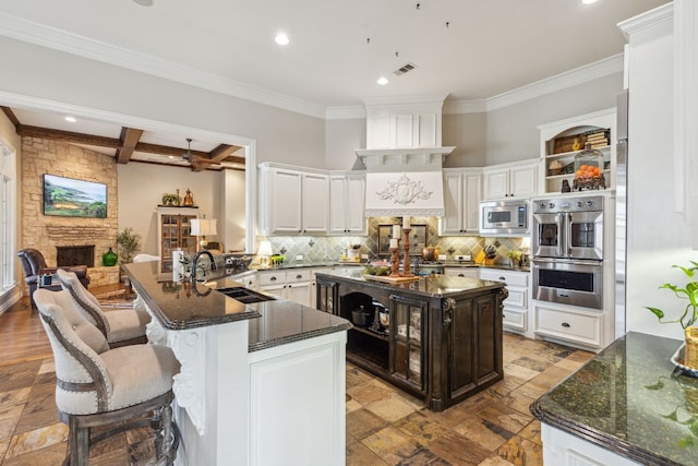 kitchen with appliances with stainless steel finishes, kitchen peninsula, a stone fireplace, sink, and ceiling fan