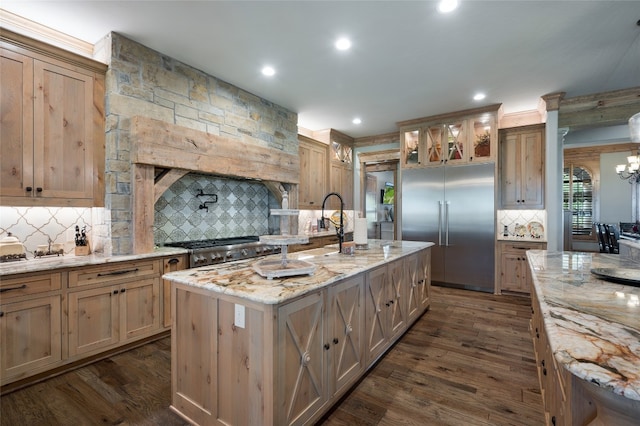 kitchen with stove, dark hardwood / wood-style floors, backsplash, and an island with sink