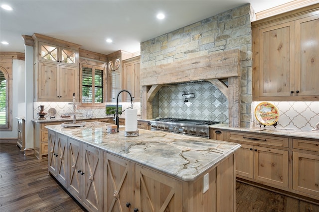 kitchen with an island with sink, light stone countertops, stove, tasteful backsplash, and dark hardwood / wood-style flooring