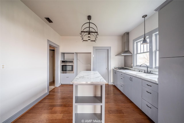 kitchen featuring sink, appliances with stainless steel finishes, hanging light fixtures, a kitchen island, and wall chimney exhaust hood