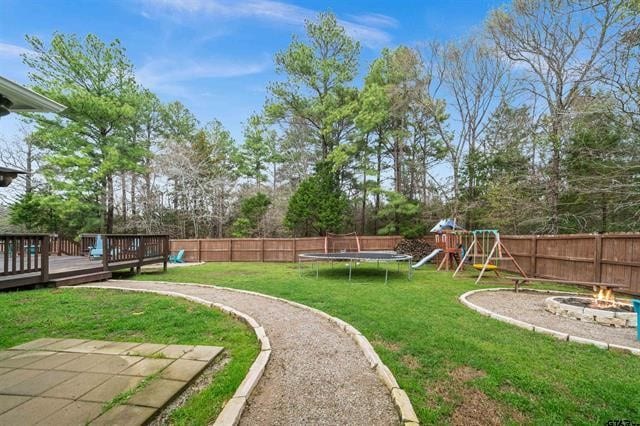 view of yard with a playground, an outdoor fire pit, a deck, and a trampoline