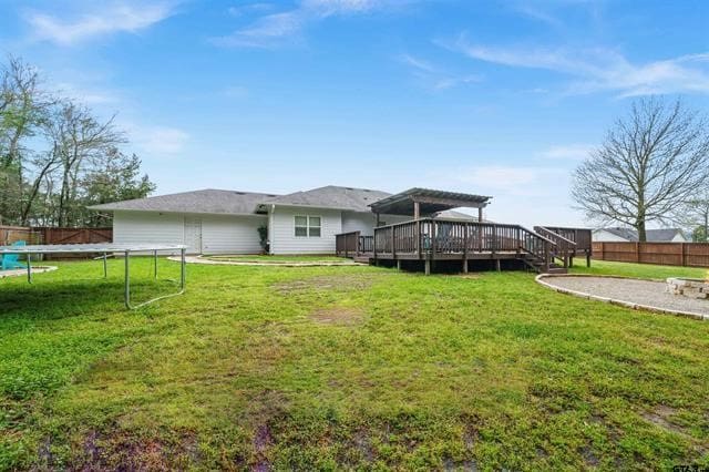 back of house featuring a lawn, a pergola, a deck, and a trampoline