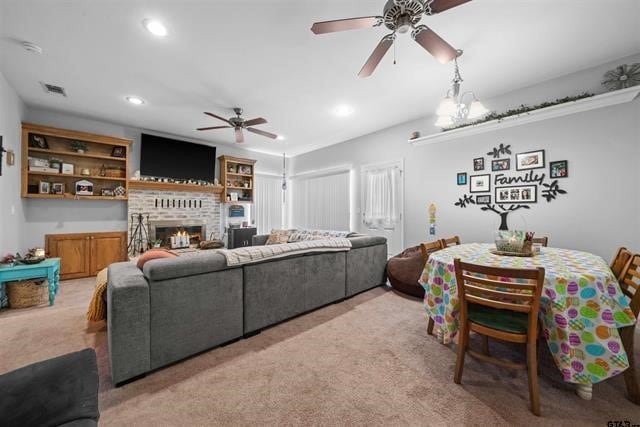 carpeted living room with ceiling fan with notable chandelier and a brick fireplace