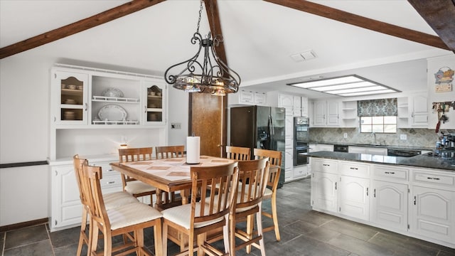 dining area with an inviting chandelier, dark tile floors, sink, and beamed ceiling