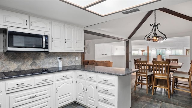 kitchen featuring white cabinets, dark stone countertops, black electric cooktop, a notable chandelier, and hanging light fixtures