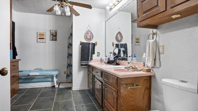 bathroom with tile floors, ceiling fan, a textured ceiling, toilet, and dual bowl vanity