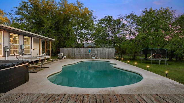 pool at dusk with a trampoline, a lawn, and a patio area