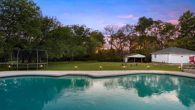 pool at dusk with a trampoline and a yard