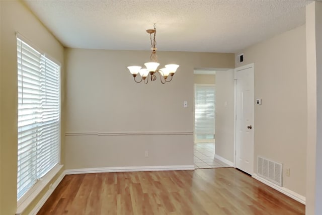 spare room featuring a textured ceiling, hardwood / wood-style flooring, a chandelier, and a healthy amount of sunlight