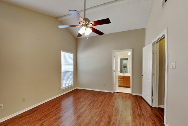 unfurnished bedroom featuring a textured ceiling, hardwood / wood-style floors, ensuite bath, lofted ceiling with beams, and ceiling fan