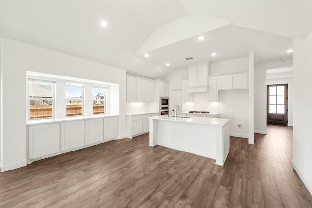 kitchen featuring lofted ceiling, sink, white cabinetry, hardwood / wood-style flooring, and a kitchen island with sink