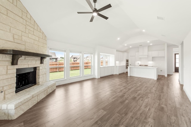 unfurnished living room featuring dark hardwood / wood-style flooring, a stone fireplace, high vaulted ceiling, and ceiling fan