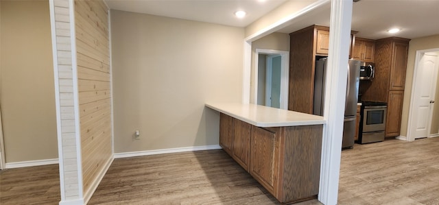 kitchen with appliances with stainless steel finishes, light hardwood / wood-style floors, and kitchen peninsula