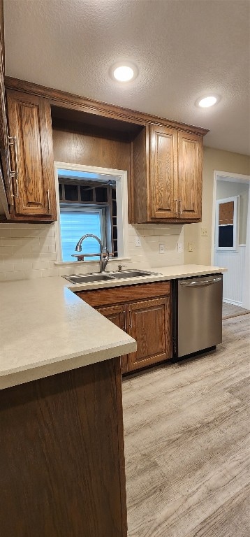 kitchen with a textured ceiling, stainless steel dishwasher, sink, and light hardwood / wood-style flooring