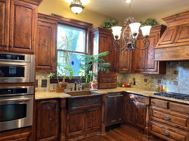 kitchen featuring dark wood-type flooring, an inviting chandelier, stainless steel appliances, light stone counters, and tasteful backsplash