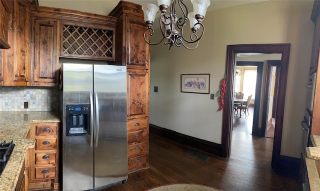 kitchen featuring stainless steel fridge with ice dispenser, dark hardwood / wood-style floors, tasteful backsplash, light stone counters, and an inviting chandelier