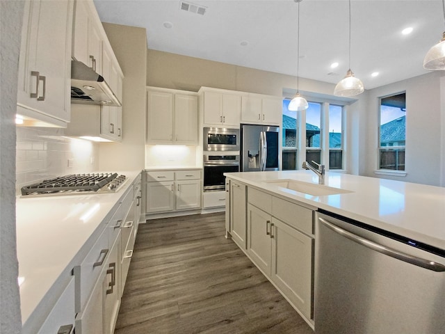 kitchen featuring pendant lighting, stainless steel appliances, wall chimney range hood, dark wood-type flooring, and white cabinets