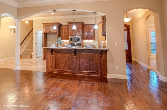 kitchen featuring dark wood-type flooring, stainless steel microwave, decorative light fixtures, ornamental molding, and decorative columns