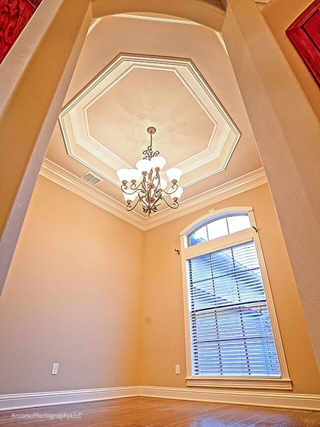 interior details featuring ornamental molding, a raised ceiling, a notable chandelier, and wood-type flooring