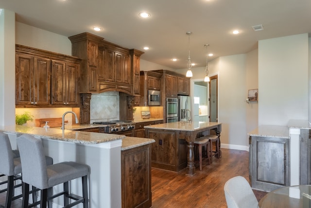 kitchen with light stone countertops, stainless steel appliances, dark hardwood / wood-style floors, kitchen peninsula, and decorative light fixtures