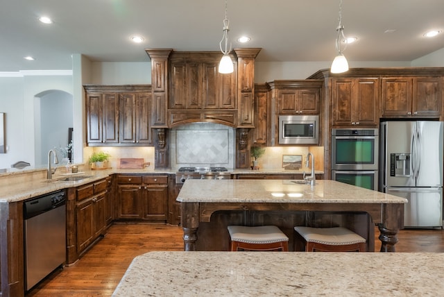 kitchen featuring tasteful backsplash, light stone counters, stainless steel appliances, sink, and decorative light fixtures