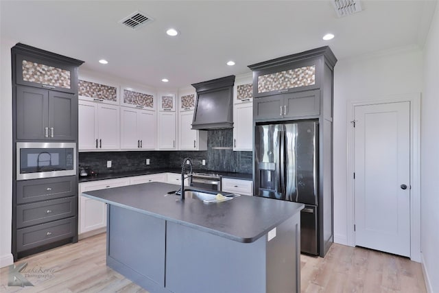 kitchen featuring sink, black microwave, an island with sink, and custom exhaust hood